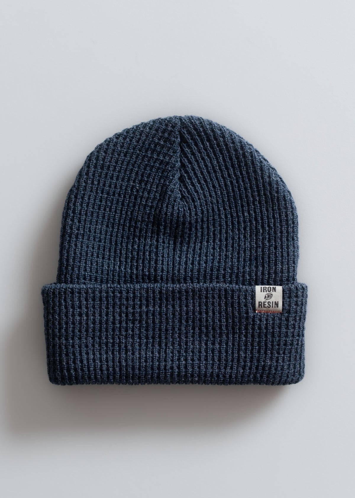 A blue knit beanie with a folded brim and an "Iron and Resin" label, displayed on a plain white background.