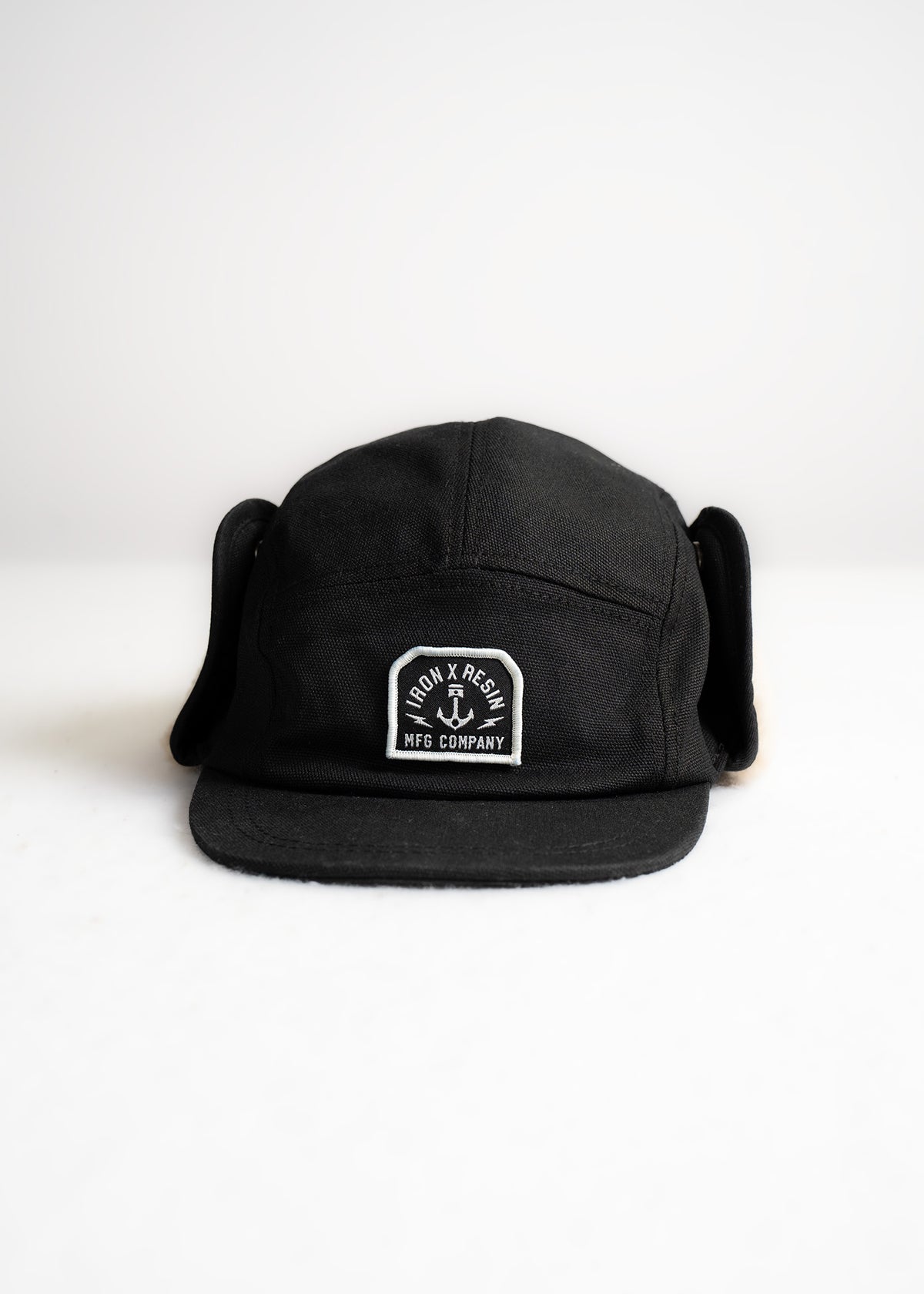 Black Iron & Resin cap with ear flaps, logo patch on front, displayed against a white background.