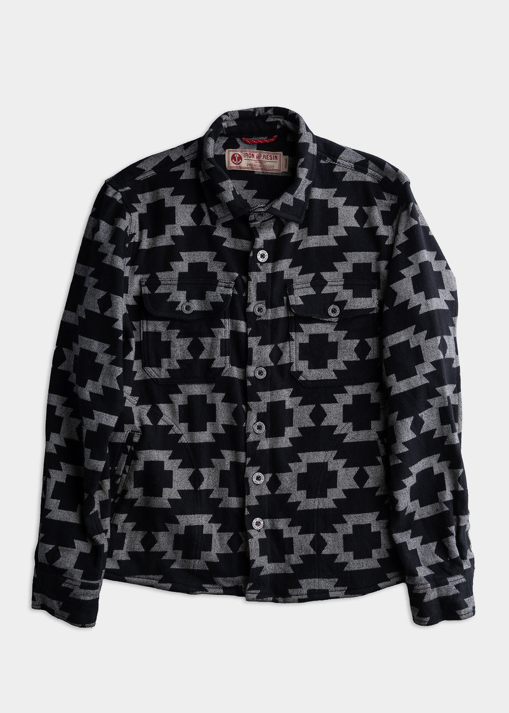 Black and grey geometric patterned shirt with buttons, featuring two chest pockets, displayed on a plain white background.