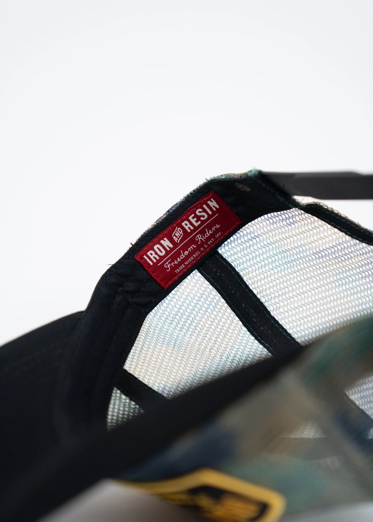 Close-up of a black mesh cap interior showing a red "Iron and Resin" label with "Freedom Riders" text, highlighting brand detail.