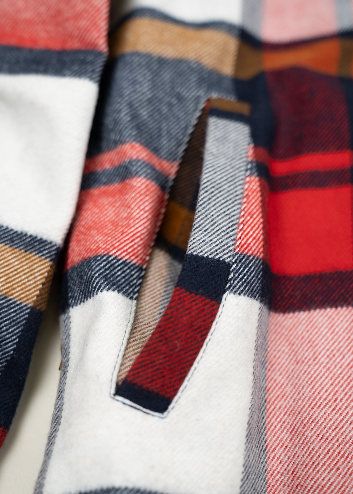 Close-up of a colorful plaid fabric with red, blue, and brown stripes, featuring a neatly sewn pocket detail.