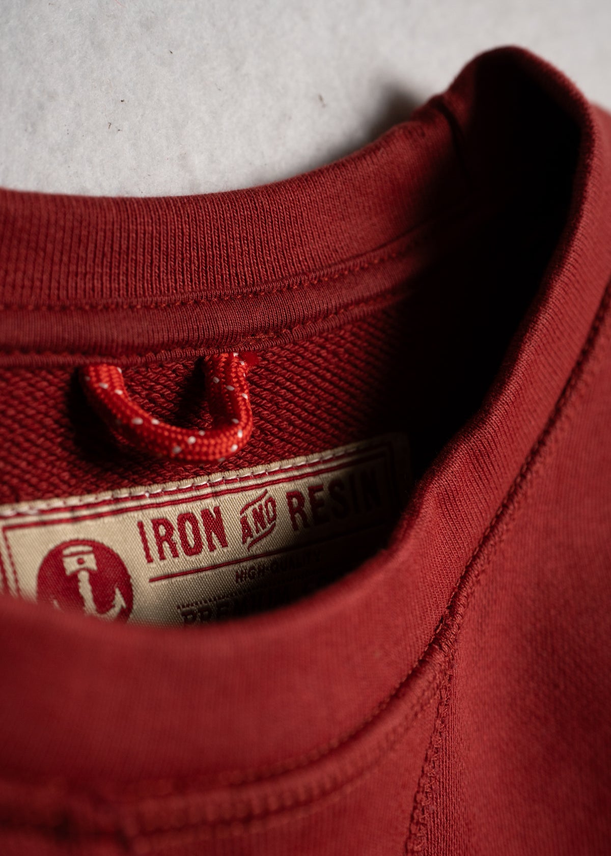 Close-up of a red sweatshirt collar with an "Iron and Resin" label, showcasing detailed stitching and fabric texture.