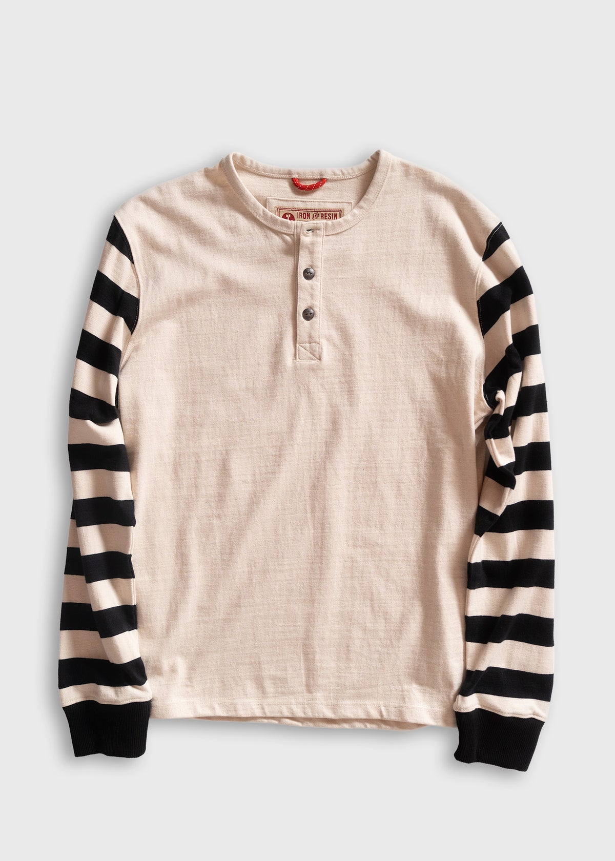 Cream henley shirt with black and white striped sleeves, featuring a three-button placket, laid flat on a white background.
