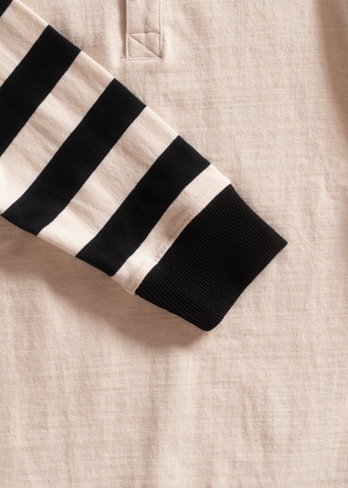 Close-up of a beige shirt with a black and white striped sleeve, featuring a ribbed cuff and a stitched detail near the collar.