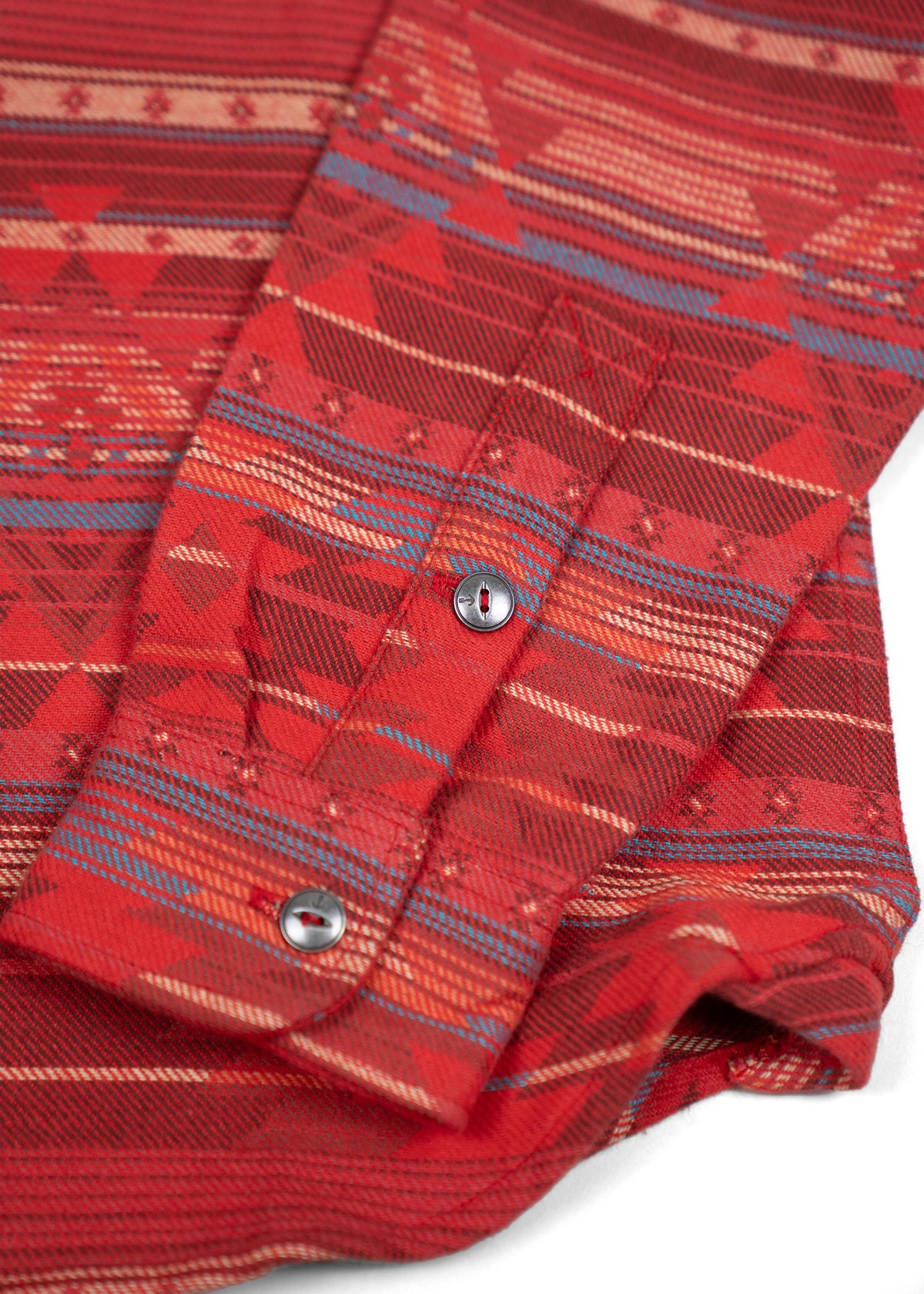 Close-up of a red shirt sleeve with geometric patterns and blue stripes, featuring two silver buttons on the cuff.