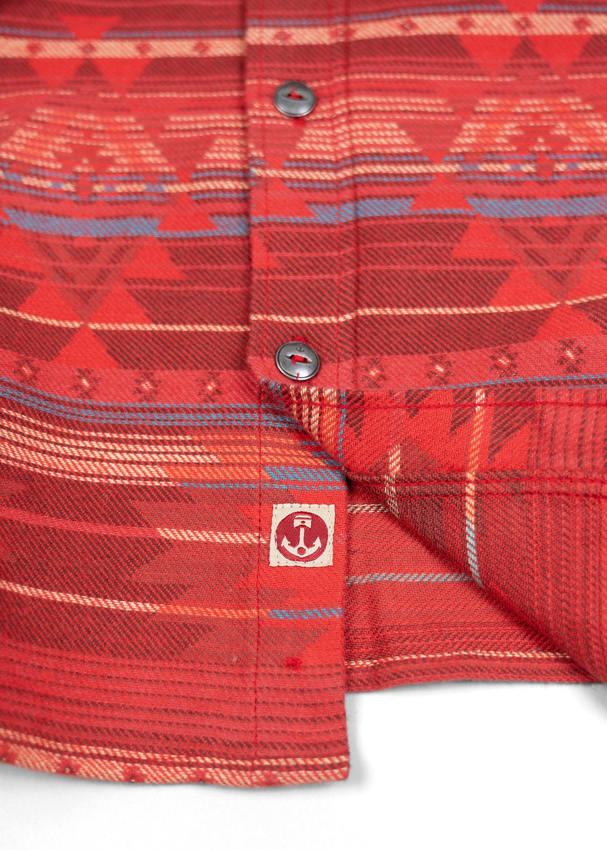 Red patterned shirt with geometric designs and metal buttons, featuring a small anchor logo tag at the bottom edge.