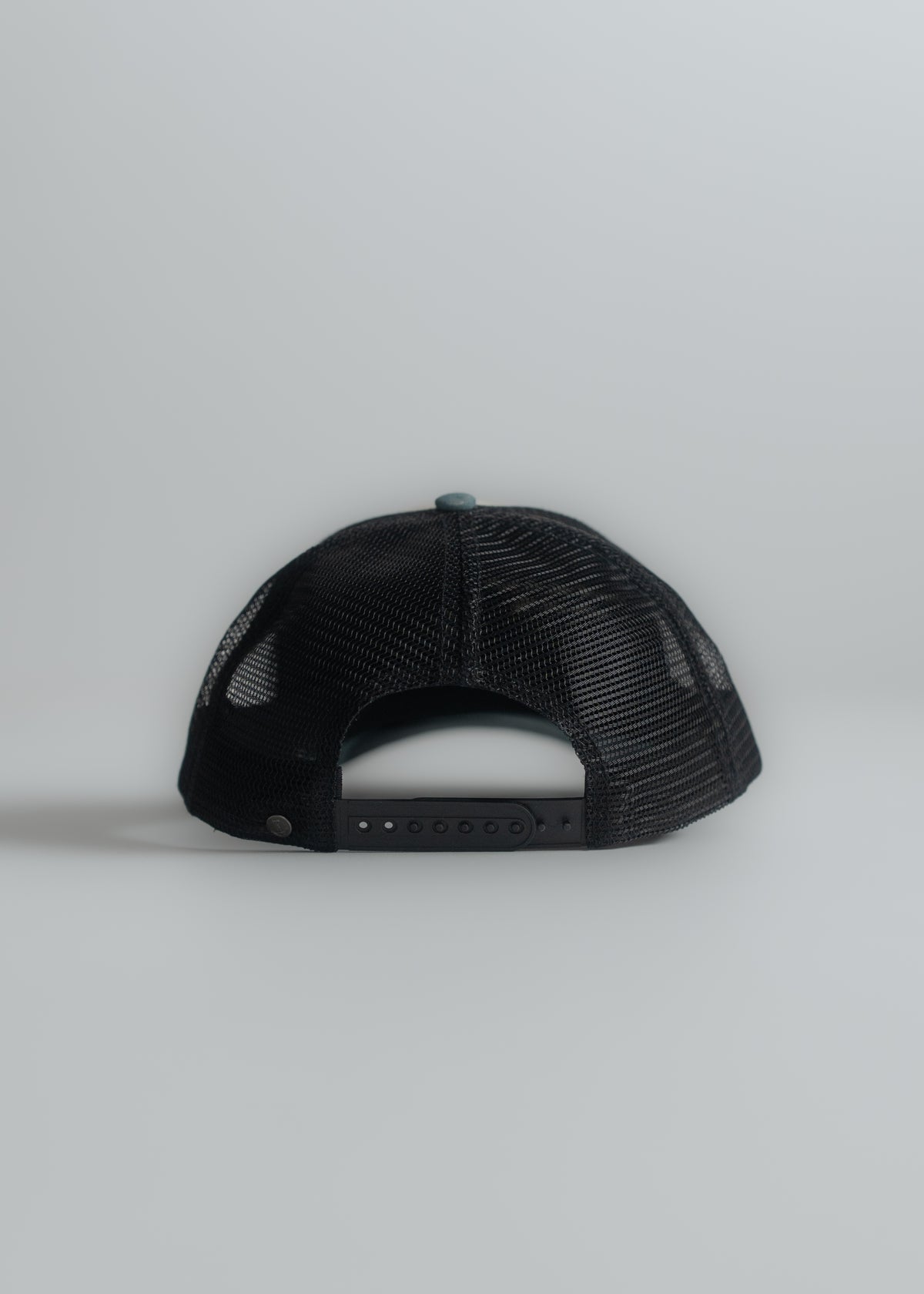 Black mesh trucker hat viewed from the back, showing adjustable strap against a light gray background.