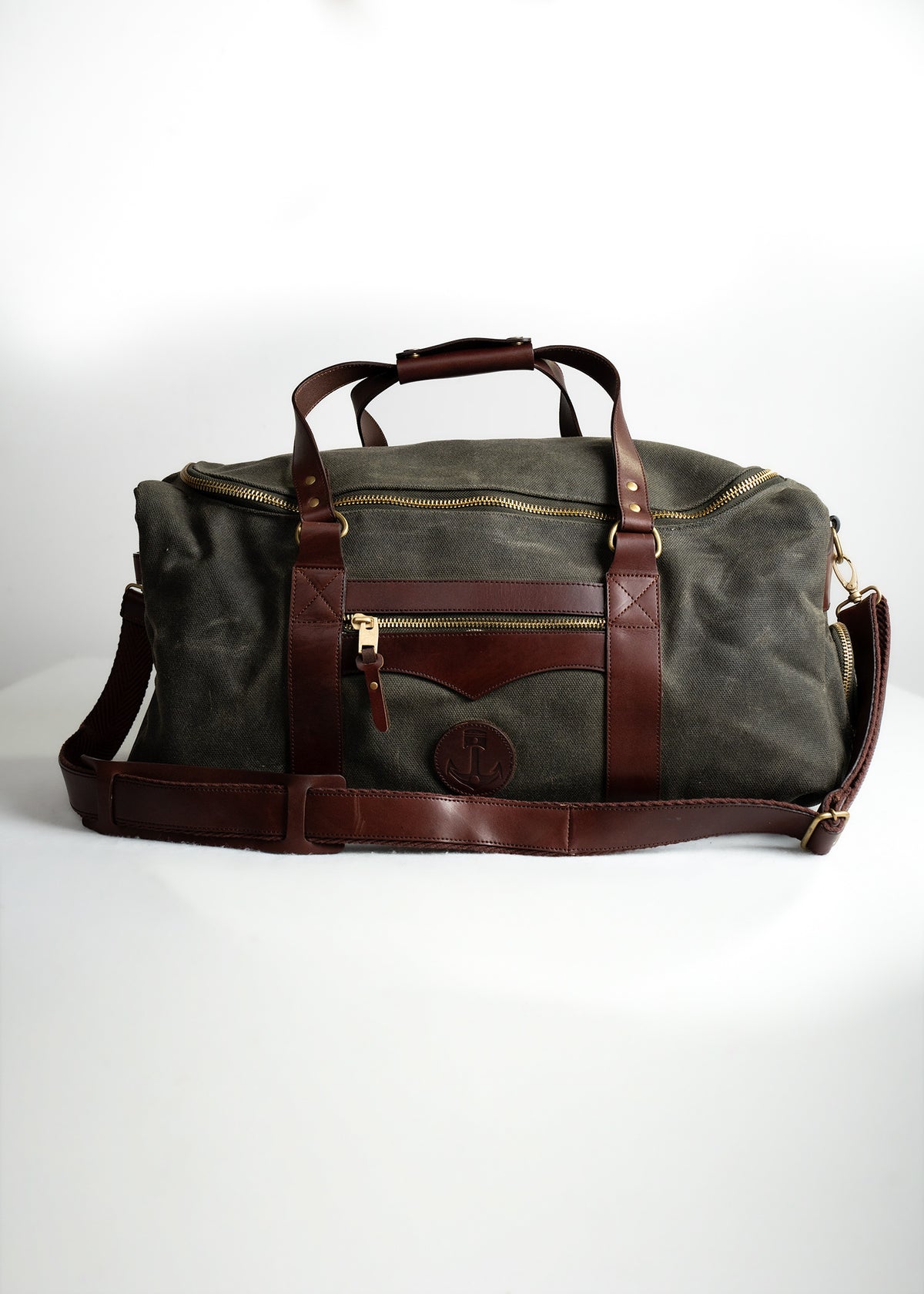 A stylish duffel bag with brown leather accents and a canvas body, featuring gold zippers and a shoulder strap on a white backdrop.