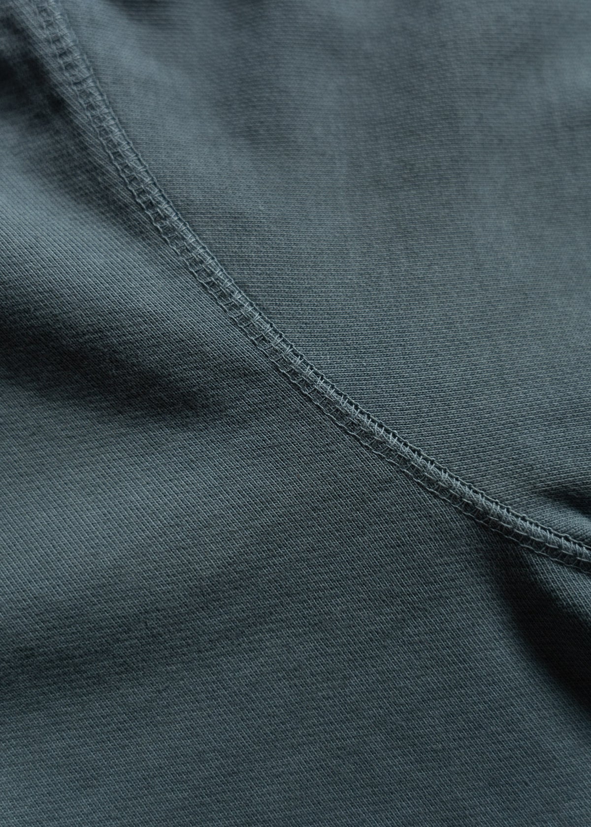 Close-up of dark gray fabric with visible stitching, showcasing texture and seam details in soft lighting.