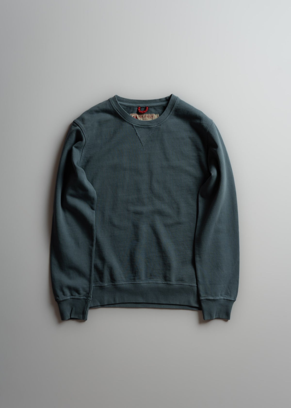 A blue crewneck sweatshirt with long sleeves lies flat on a light gray surface, showcasing its simple, casual design.