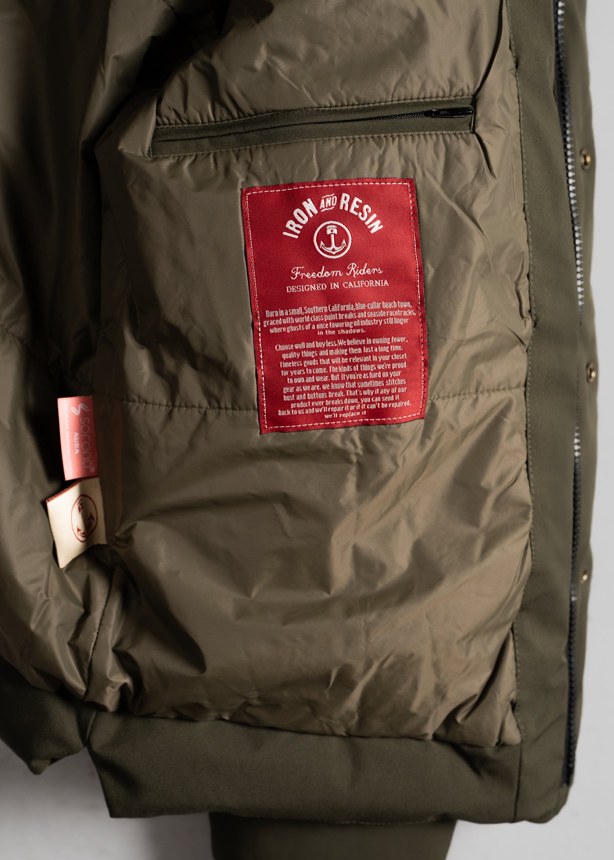 Close-up of a jacket's interior showing a red "Iron and Resin" label with text, highlighting its California design origin.