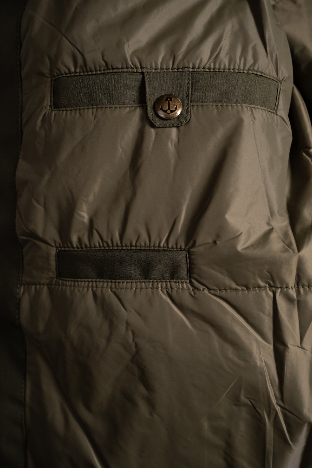 Close-up of a dark green jacket with a buttoned flap and stitched pocket detail, highlighting its texture and design elements.