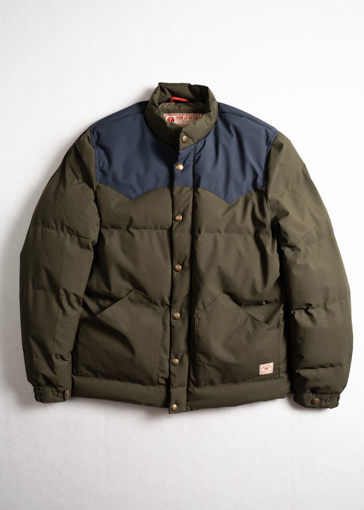 Green and navy puffer jacket with button closure, featuring two front pockets, displayed against a plain white background.