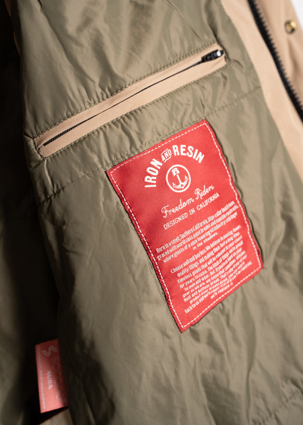 Close-up of a jacket's inner label reading "Iron and Resin, Freedom Riders, Designed in California" with a zippered pocket above.