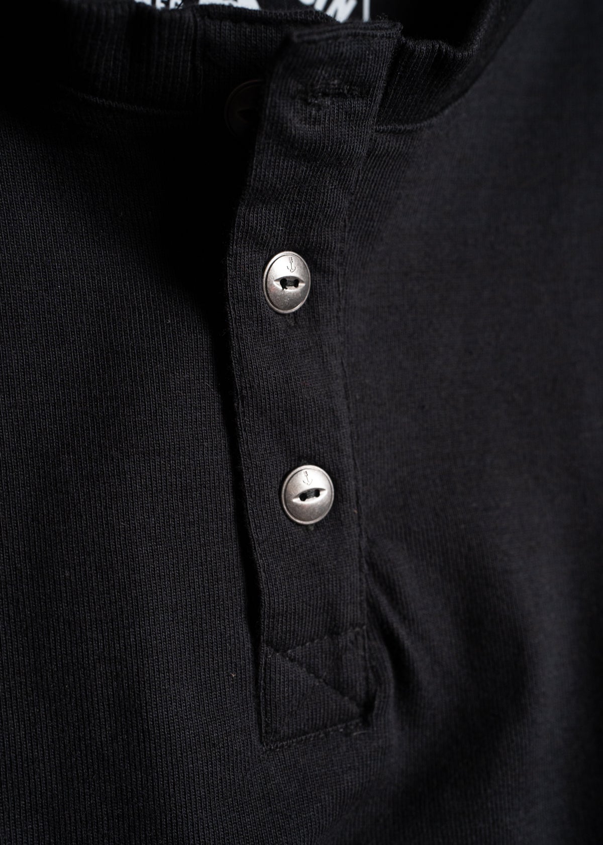 Close-up of a black henley shirt with two metal buttons, highlighting the textured fabric and button details.
