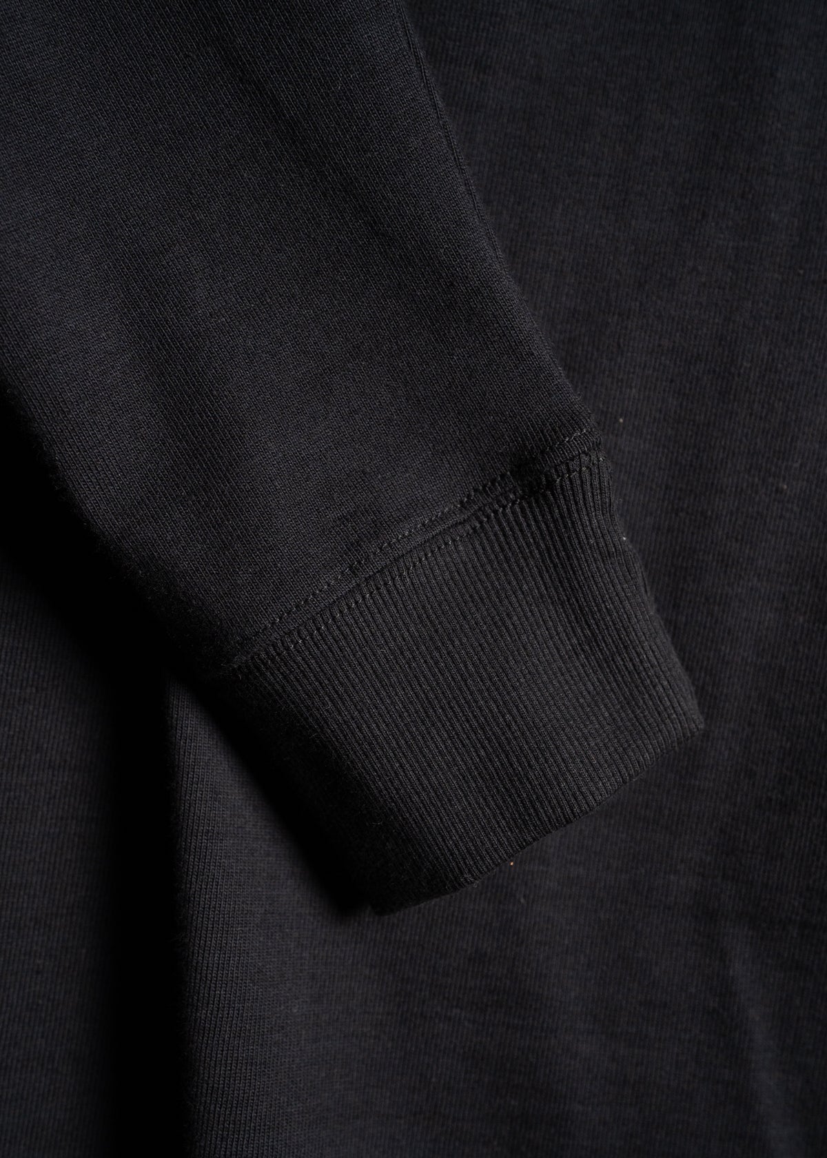 Close-up of a black sweatshirt sleeve showing ribbed cuff detail, highlighting the texture and fabric quality.