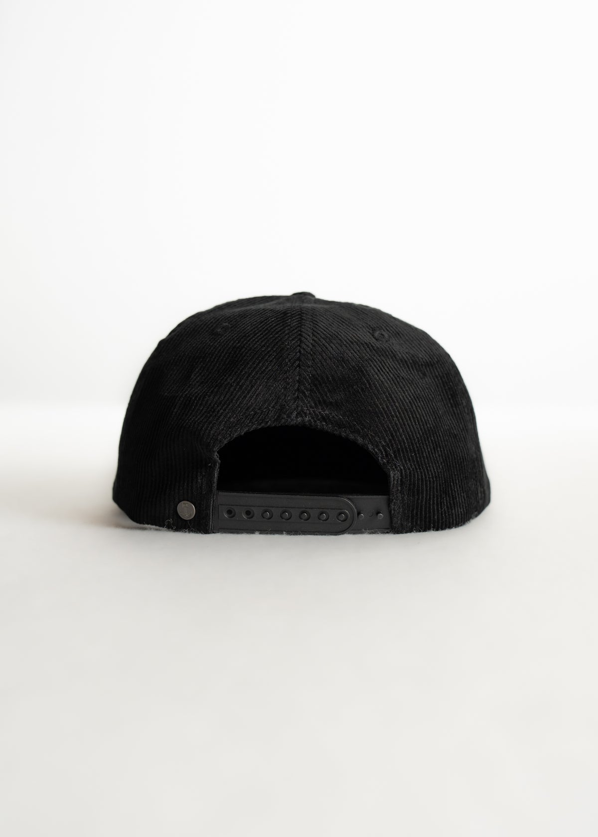 A black corduroy baseball cap with an adjustable strap is centered against a plain white background, showcasing its back view.