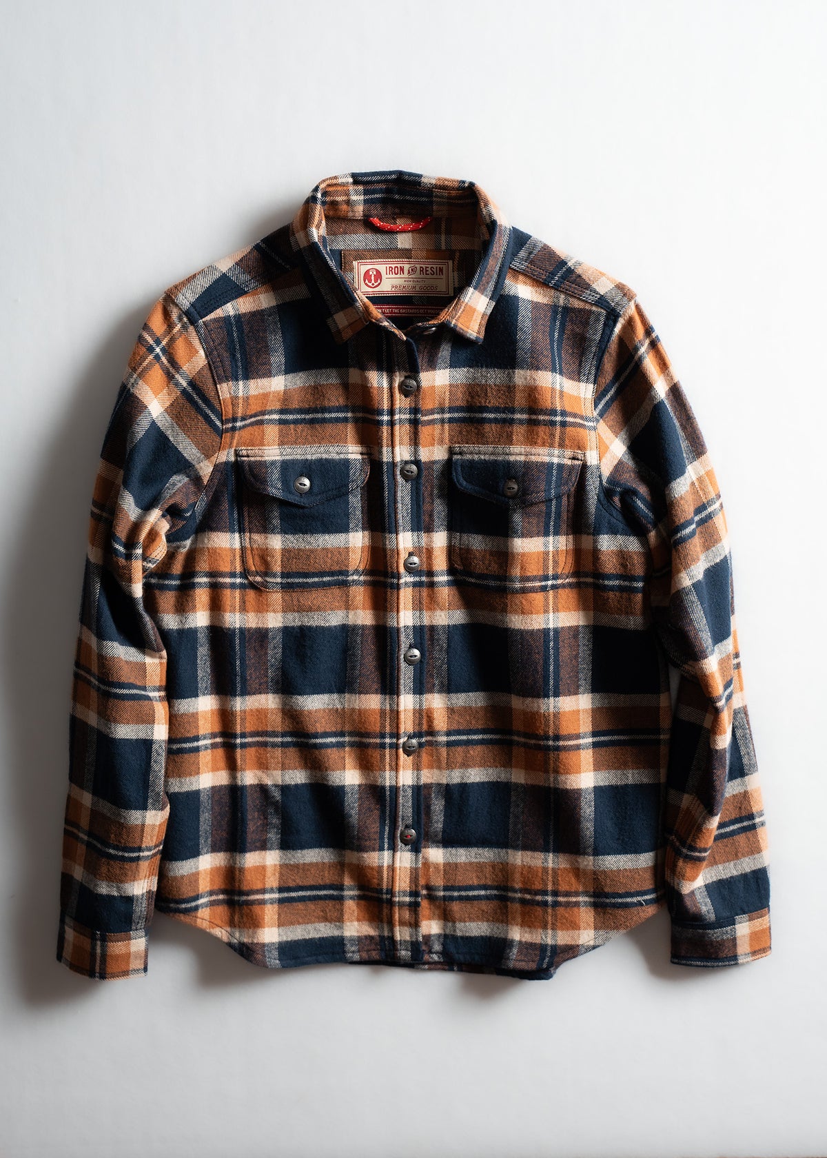 Plaid flannel shirt in blue and orange tones, featuring button closure and two chest pockets, laid flat on a white background.
