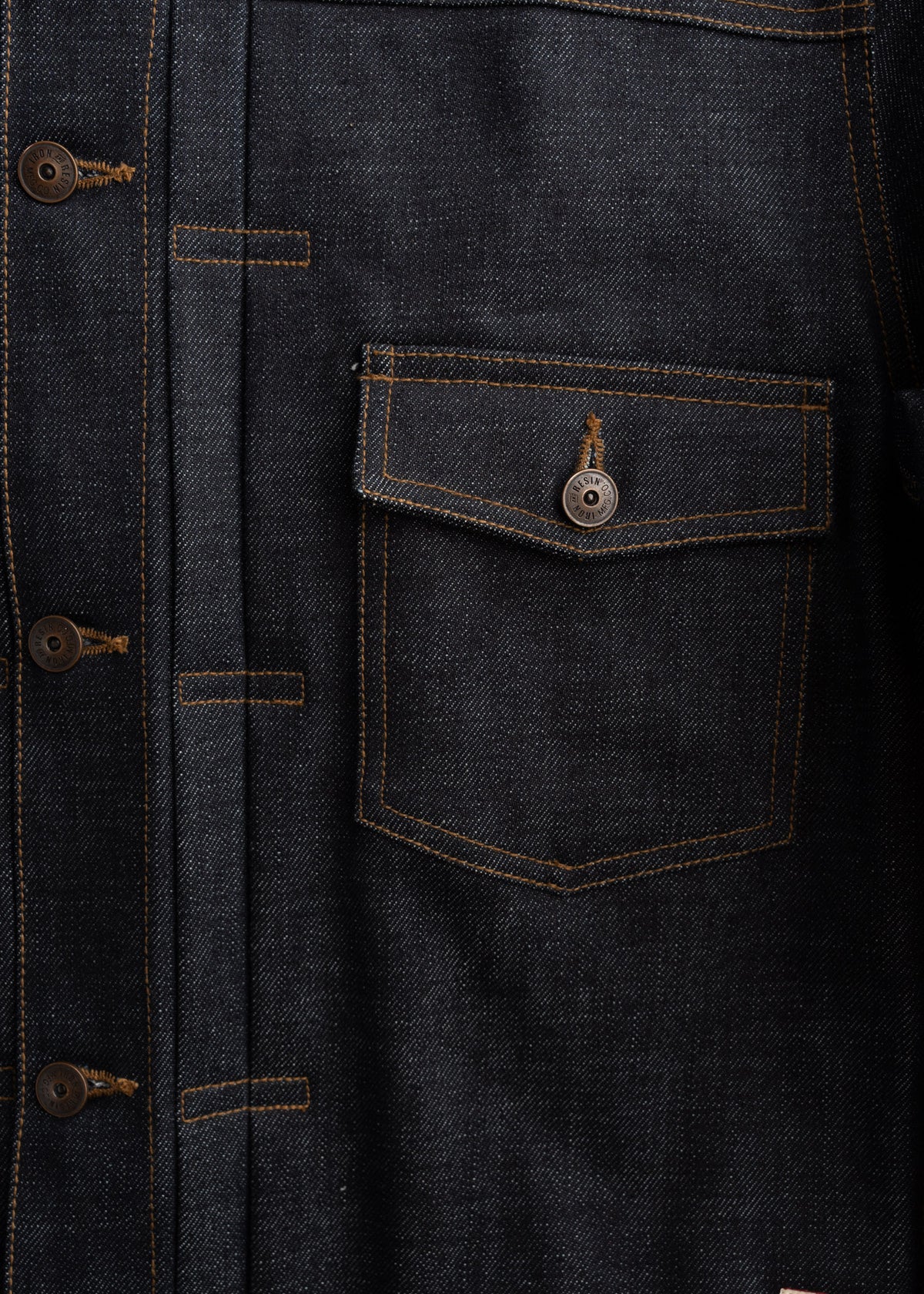 Close-up of a dark denim jacket with brown buttons and a buttoned pocket, showcasing detailed stitching and texture.