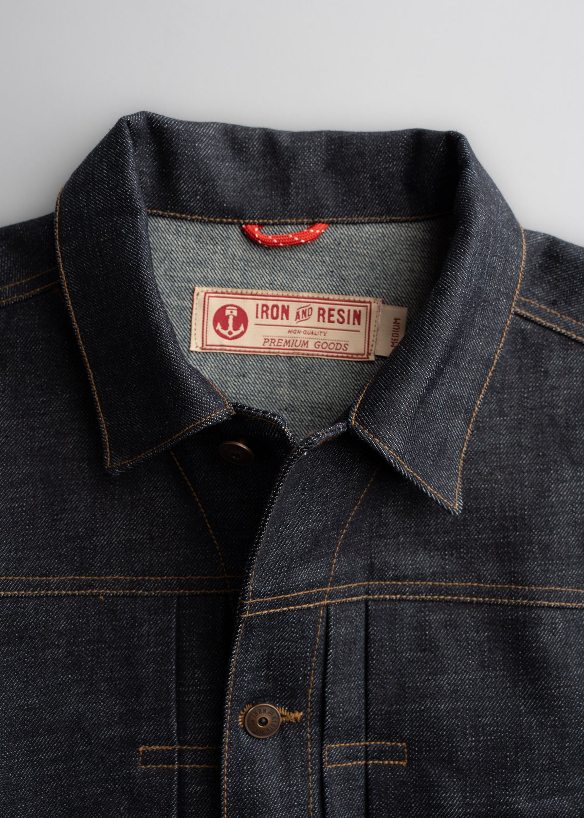 Dark denim jacket with visible stitching and a label reading "Iron and Resin Premium Goods" on the collar, buttoned up.