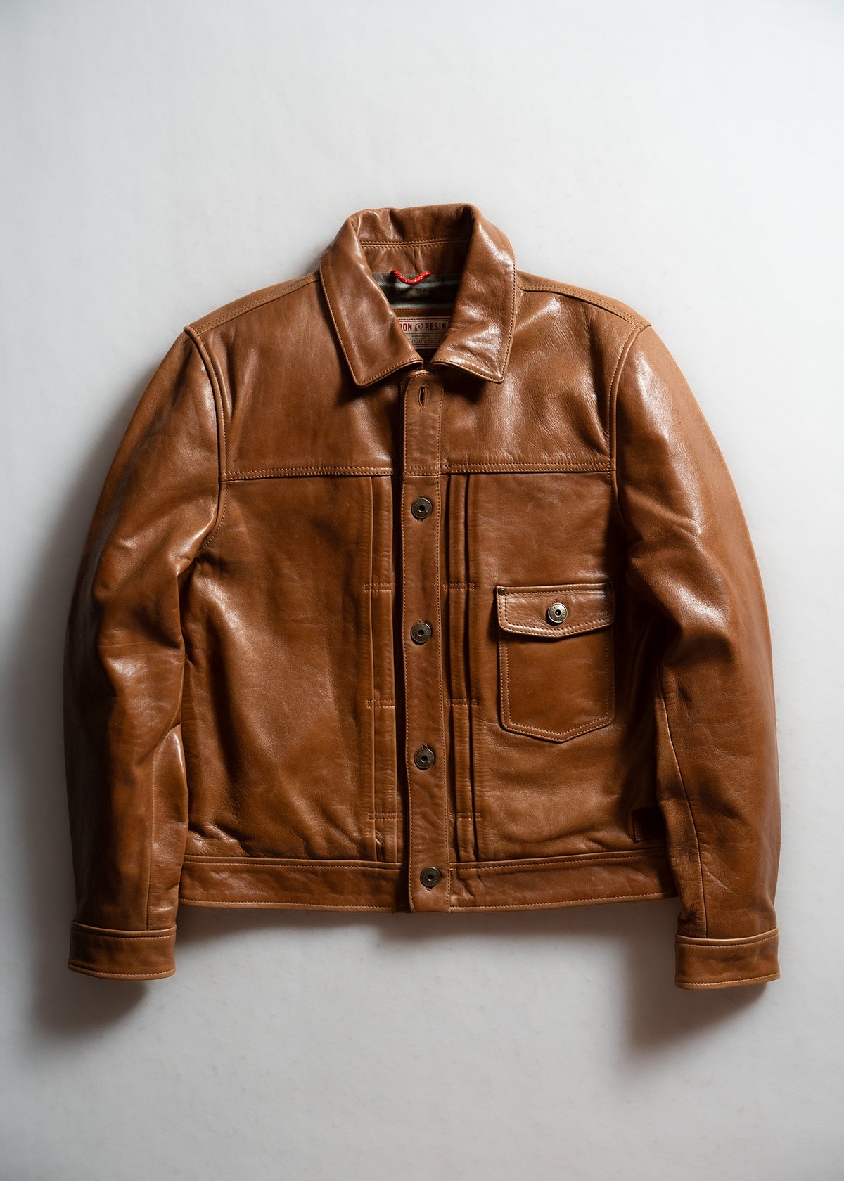 Brown leather jacket with button front and pocket, displayed on a white background, showcasing its classic style and texture.