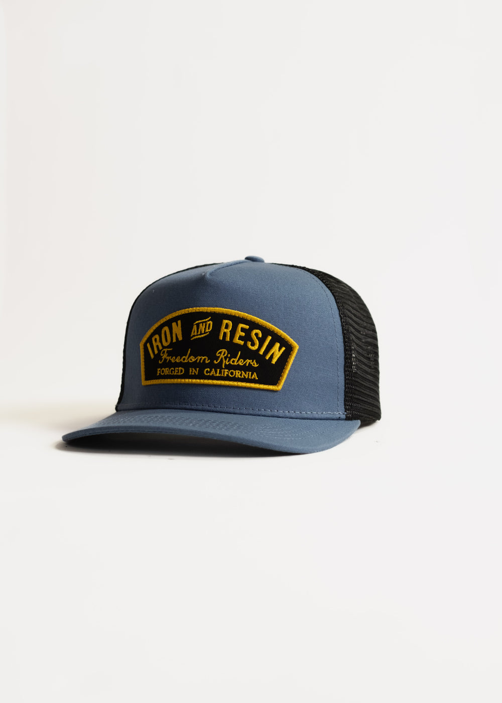 Blue and black trucker hat with "Iron and Resin, Freedom Riders, Forged in California" patch on front, isolated on white.