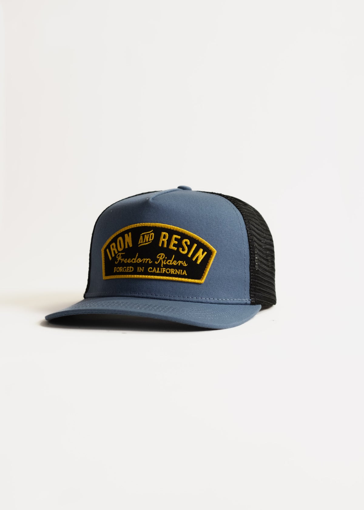 Blue and black trucker hat with "Iron and Resin, Freedom Riders, Forged in California" patch on front, isolated on white.