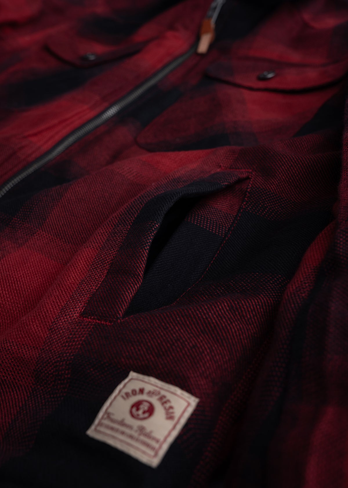 Close-up of a red and black plaid jacket with a zipper and pocket, featuring an Iron & Resin label on the fabric.