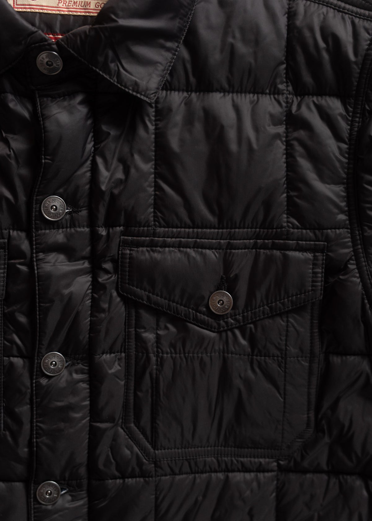 Close-up of a black quilted jacket with buttons and a chest pocket, showcasing its shiny texture and detailed stitching.