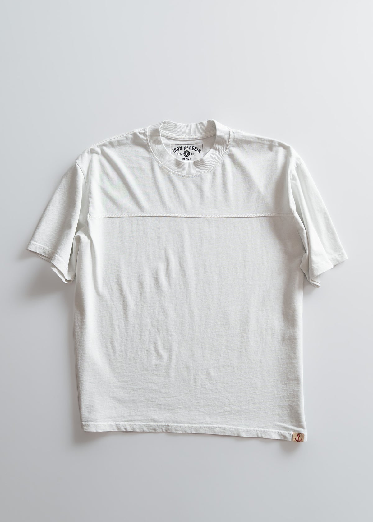 White T-shirt on a light background, featuring a round neck and short sleeves. The label reads "Iron & Resin" with a small anchor logo.