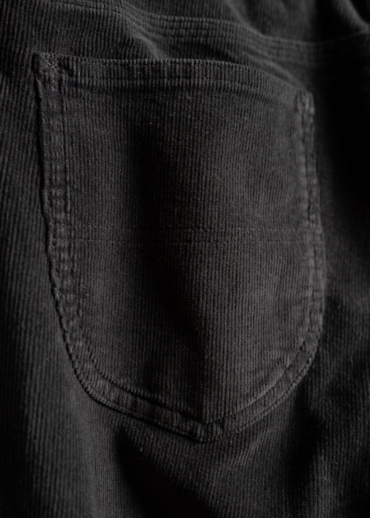 Close-up of a black corduroy fabric pocket, showing detailed texture and stitching, highlighting the material's soft, ribbed surface.