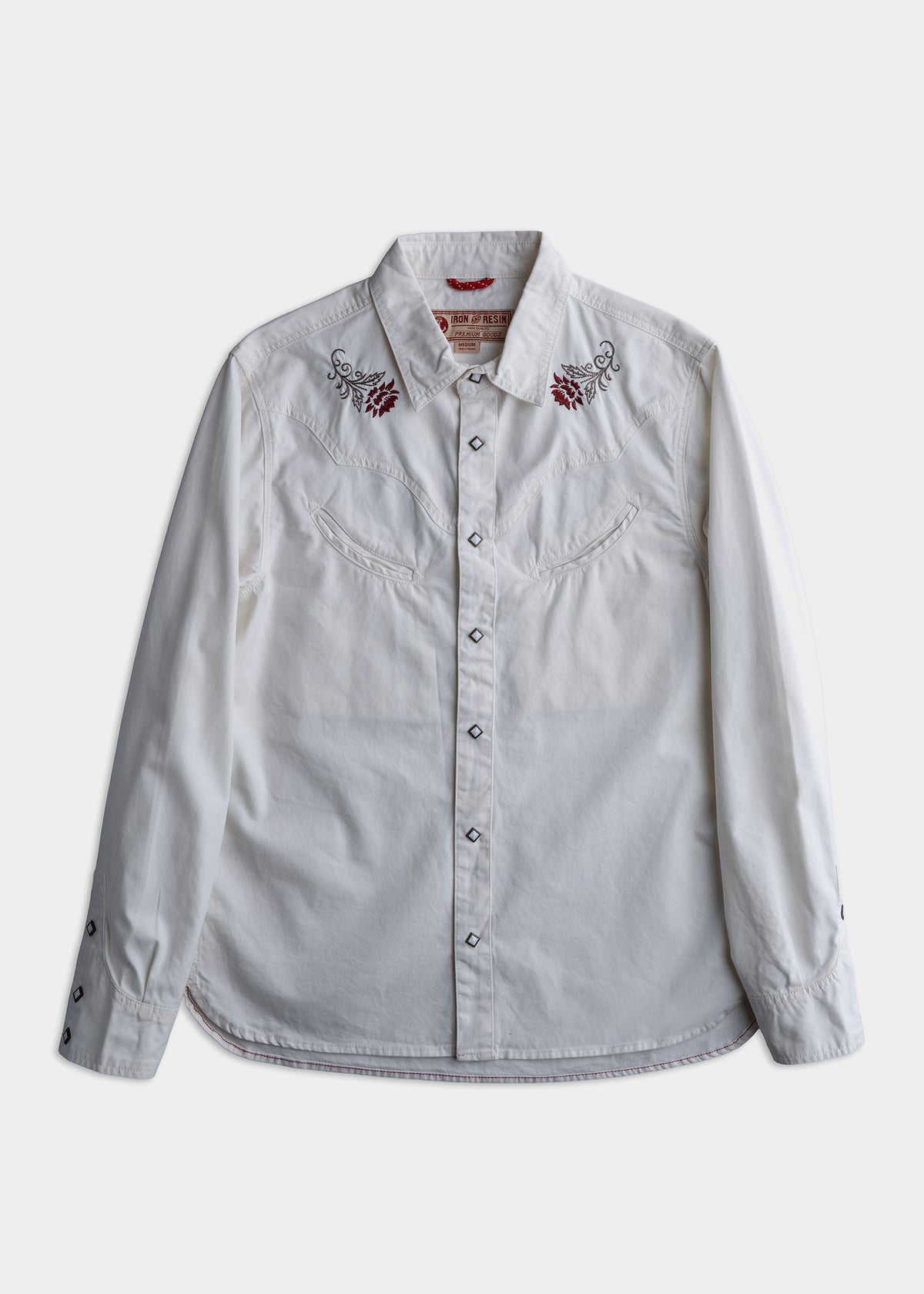White western shirt with red floral embroidery on the shoulders, featuring snap buttons and a pointed collar, laid flat on a surface.
