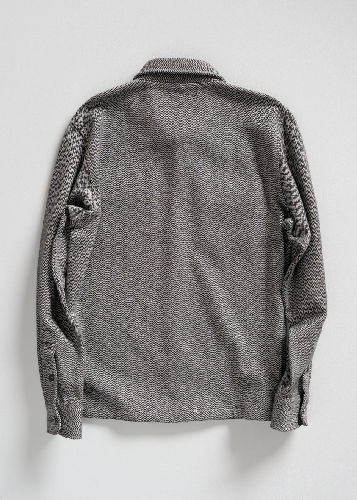 Gray herringbone-patterned shirt viewed from the back, featuring long sleeves and a classic collar against a plain background.