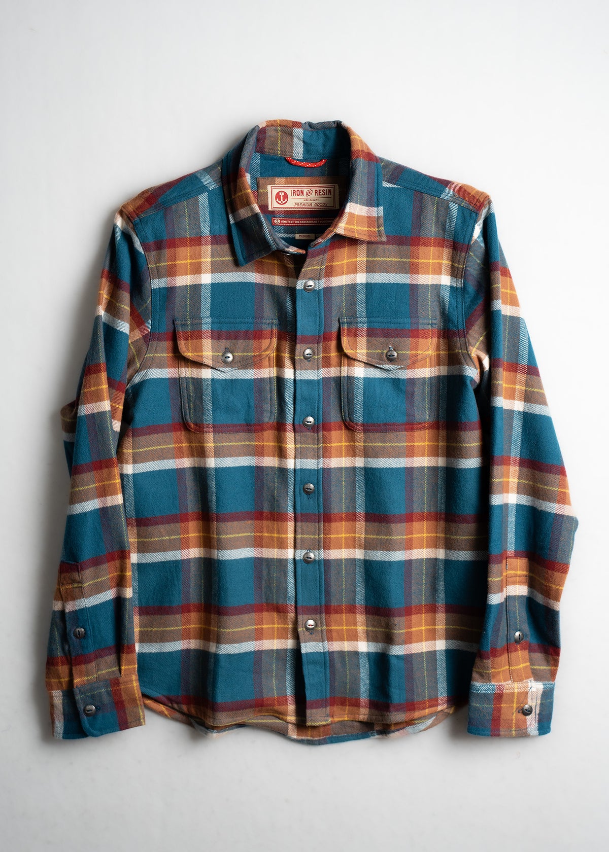 Plaid flannel shirt with blue, red, and yellow checks, featuring buttoned pockets, laid flat on a white background.