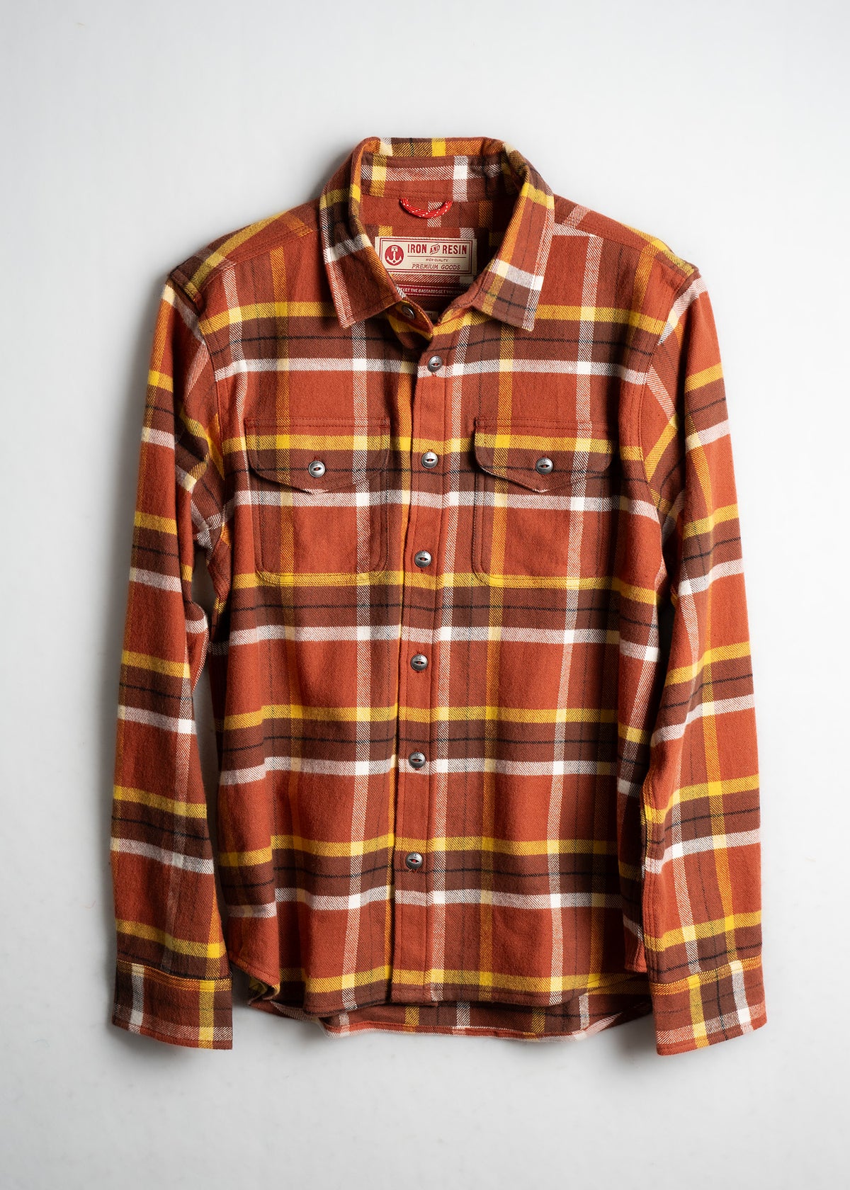 Orange, yellow, and brown plaid flannel shirt with buttons, two chest pockets, and a collar, displayed on a white background.