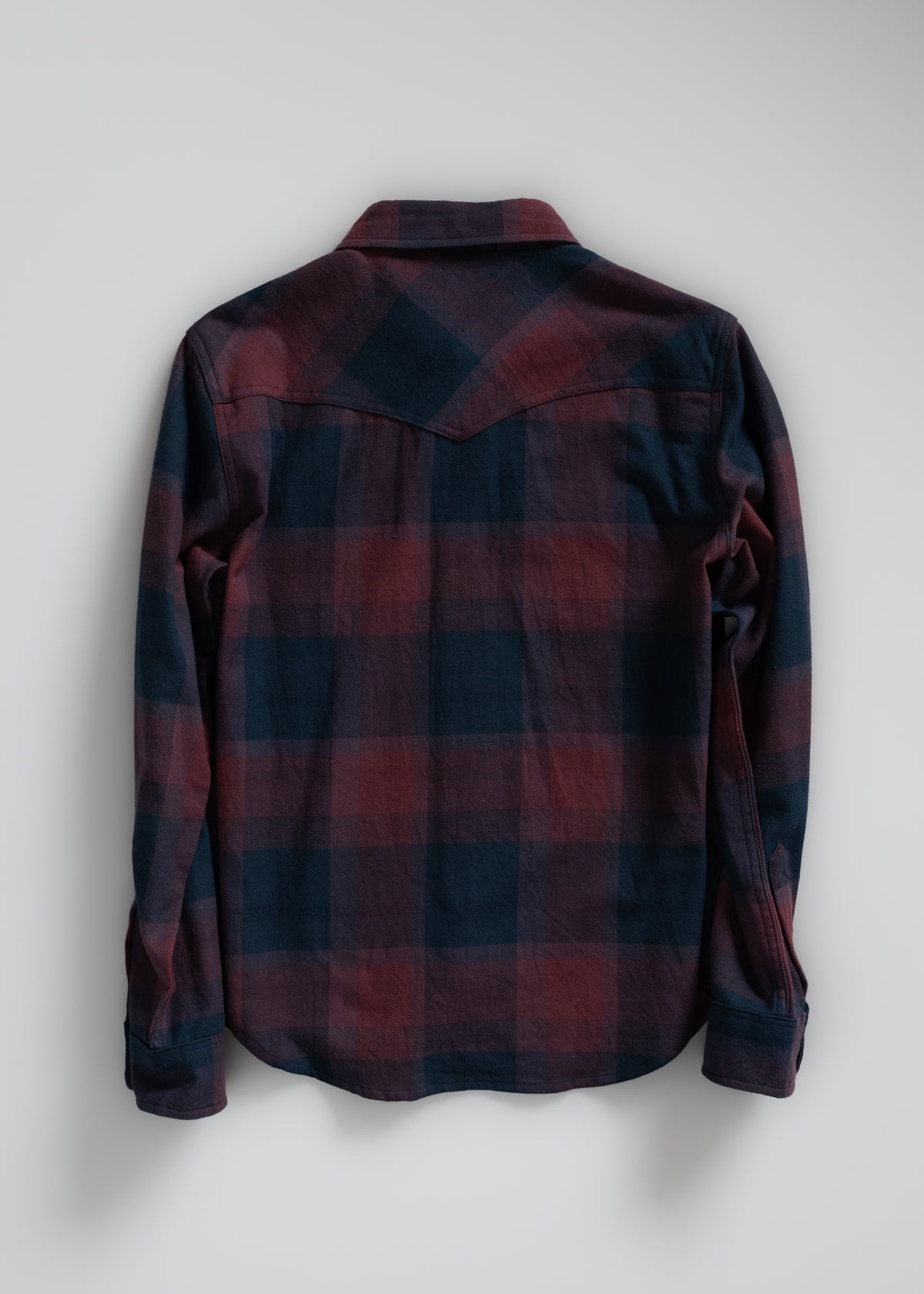 Back view of a long-sleeve, red and blue plaid flannel shirt on a plain background, showcasing its casual style and pattern.
