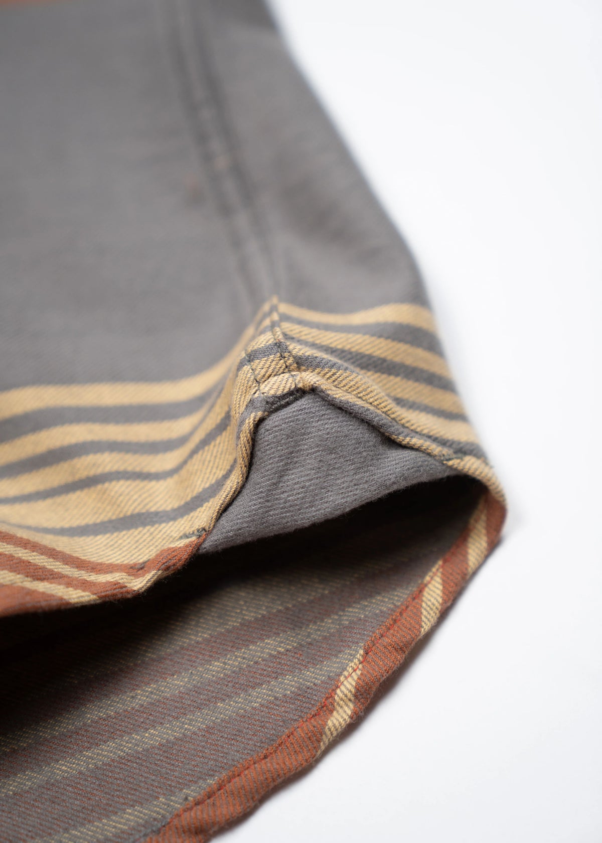 Close-up of a folded grey fabric with yellow and brown stripes, showcasing detailed stitching and texture on a white background.