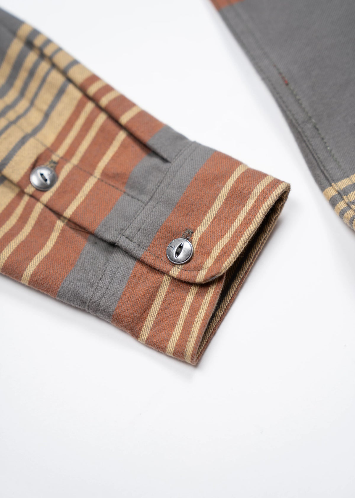 Close-up of a striped shirt sleeve with metal buttons, featuring shades of brown and gray on a white background.