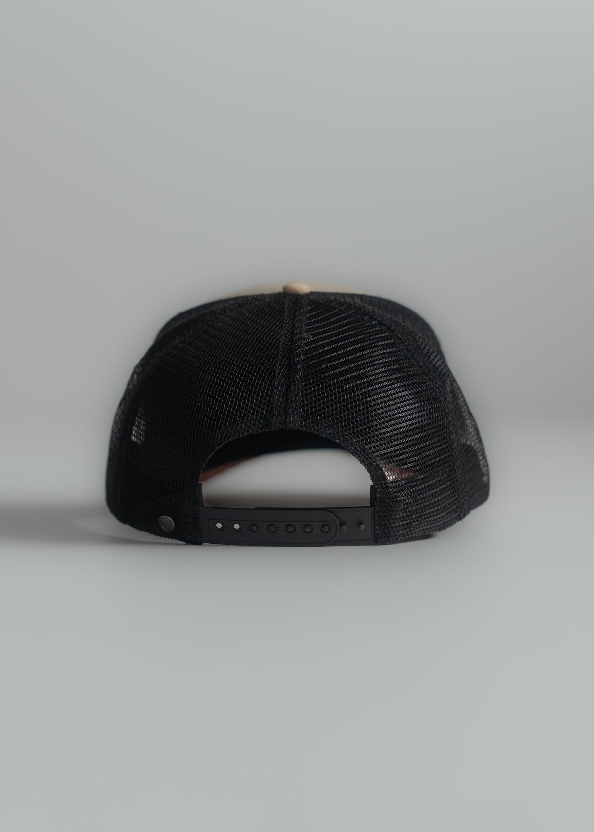 Black mesh trucker cap with adjustable strap, viewed from the back against a plain gray background.