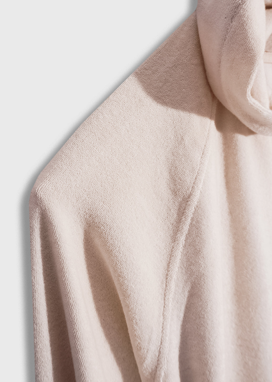 Close-up of a beige textured hoodie, showcasing its soft fabric and subtle shadowing, highlighting the garment's cozy appeal.