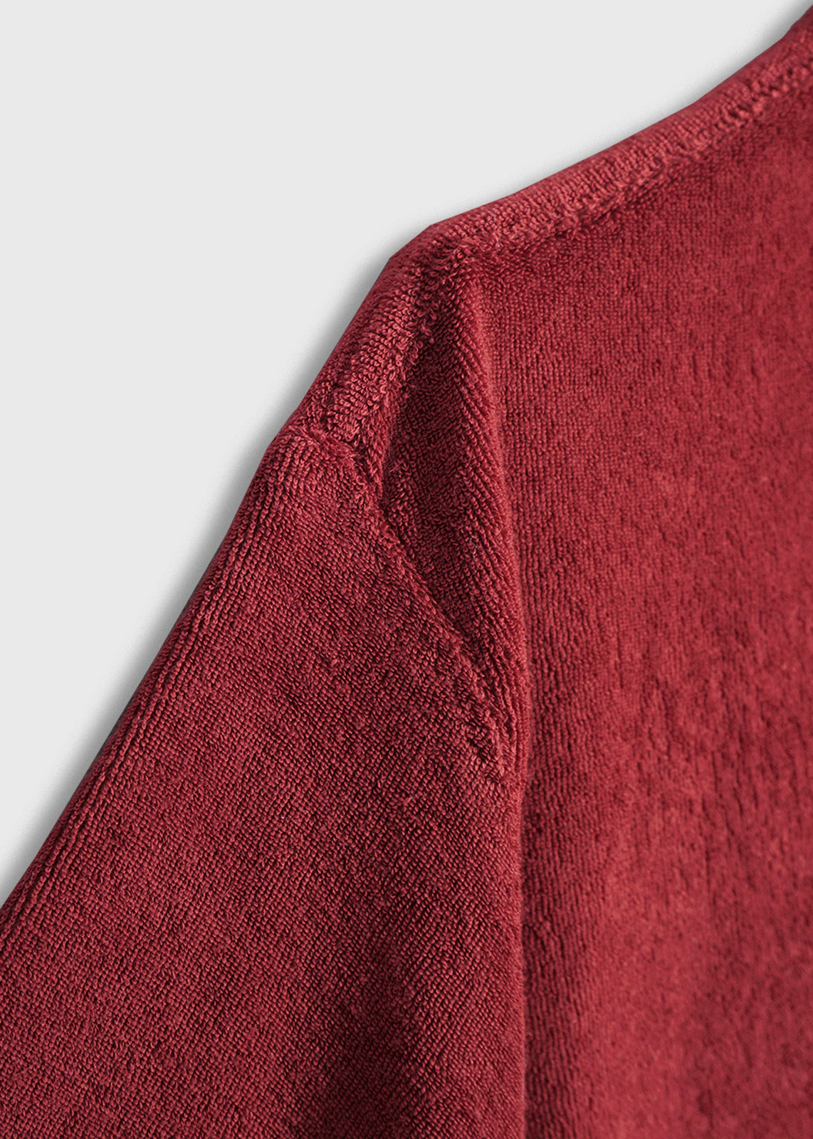 Close-up of a red terry cloth fabric showing detailed texture and stitching on a garment's shoulder against a light background.
