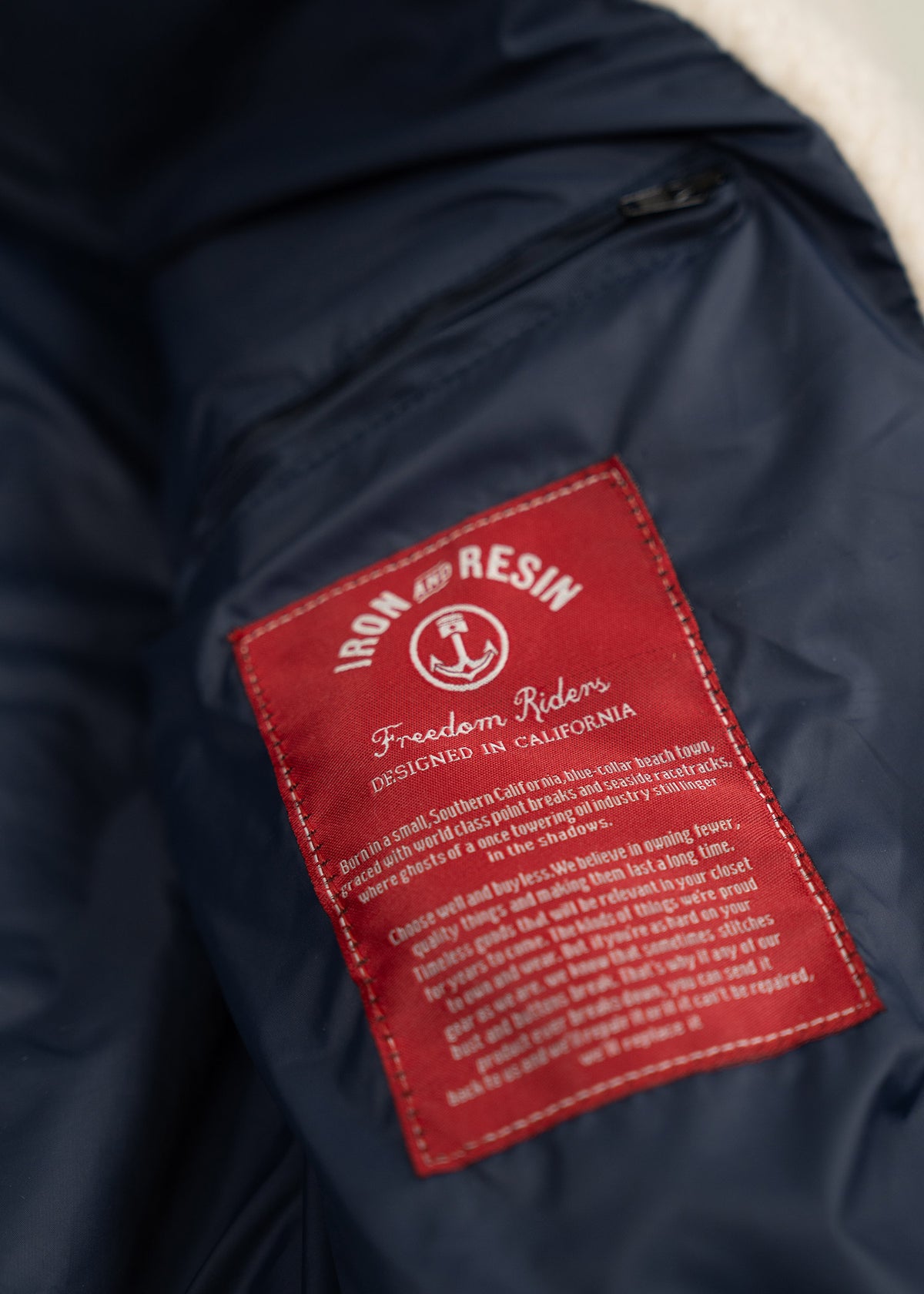 Red "Iron and Resin" label on a navy jacket, reading "Freedom Riders, Designed in California," with detailed text below.