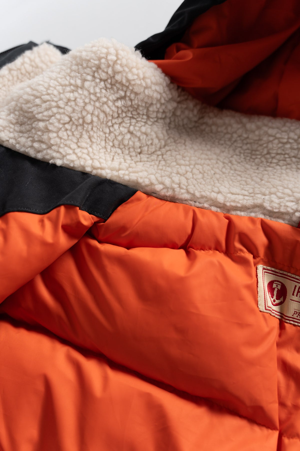 Close-up of an orange jacket with a soft, cream fleece lining and a visible label, highlighting warmth and comfort.