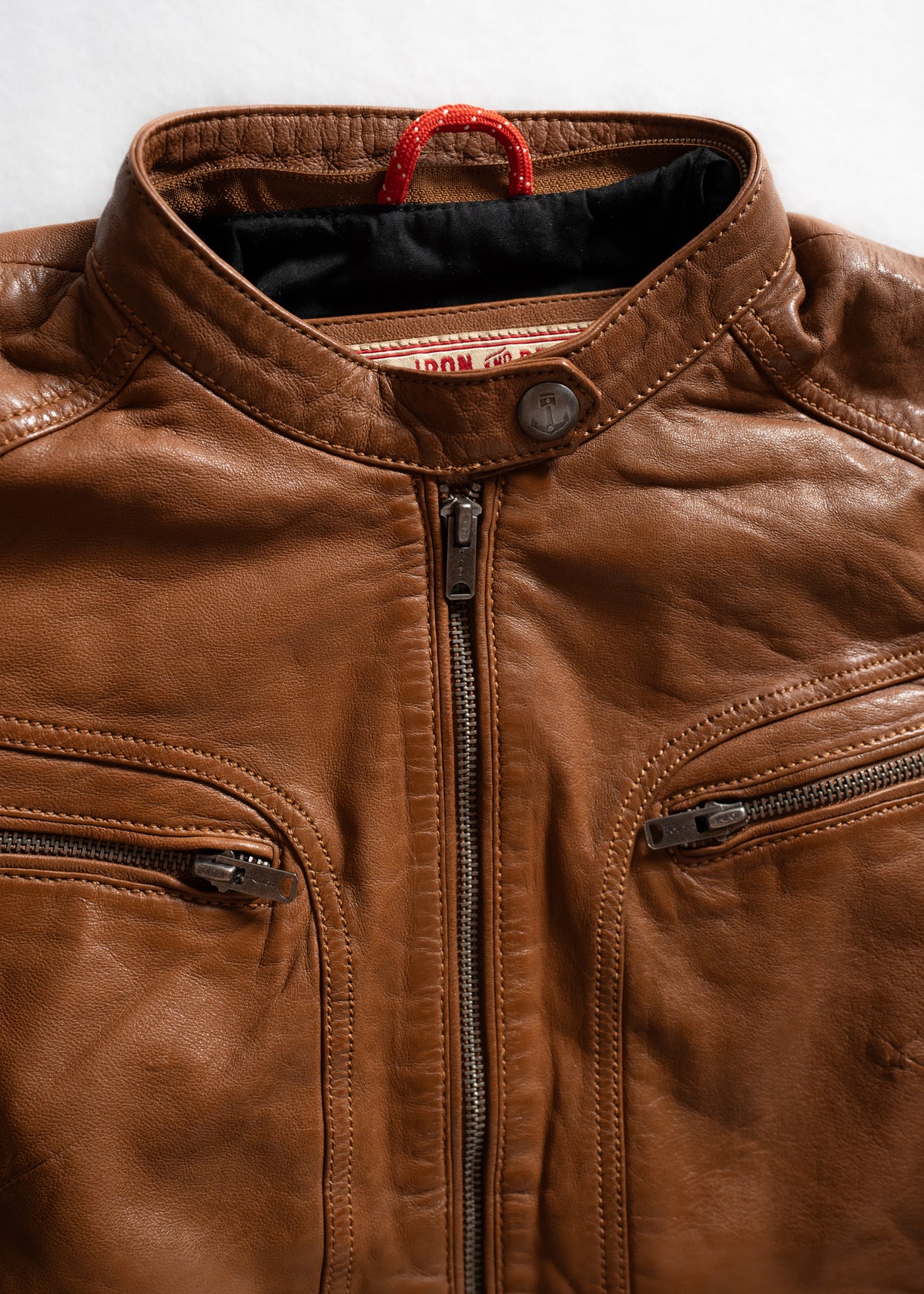 Brown leather jacket with a high collar and two zippered chest pockets, showcasing a rugged, stylish design on a light background.