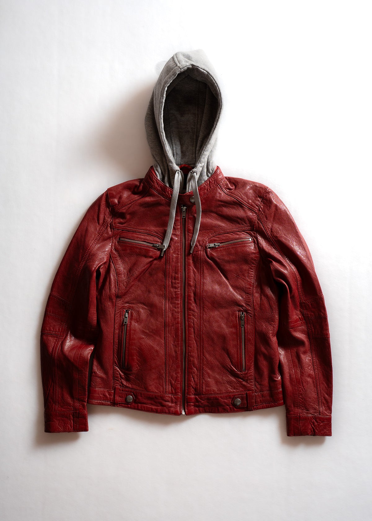 Red leather jacket with gray hoodie on white background, featuring zippered pockets and a casual, stylish design.
