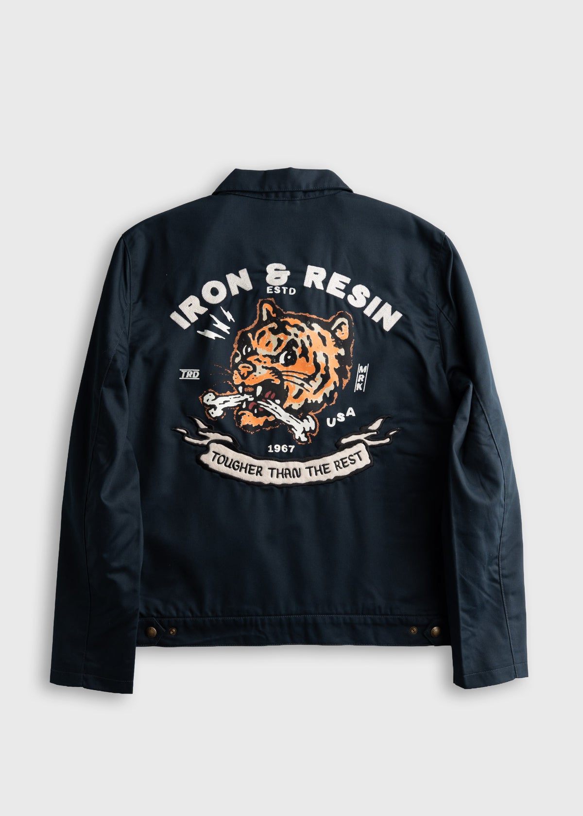 Navy jacket back with a fierce tiger design, "Iron & Resin," and "Tougher Than The Rest" text in bold white and orange.