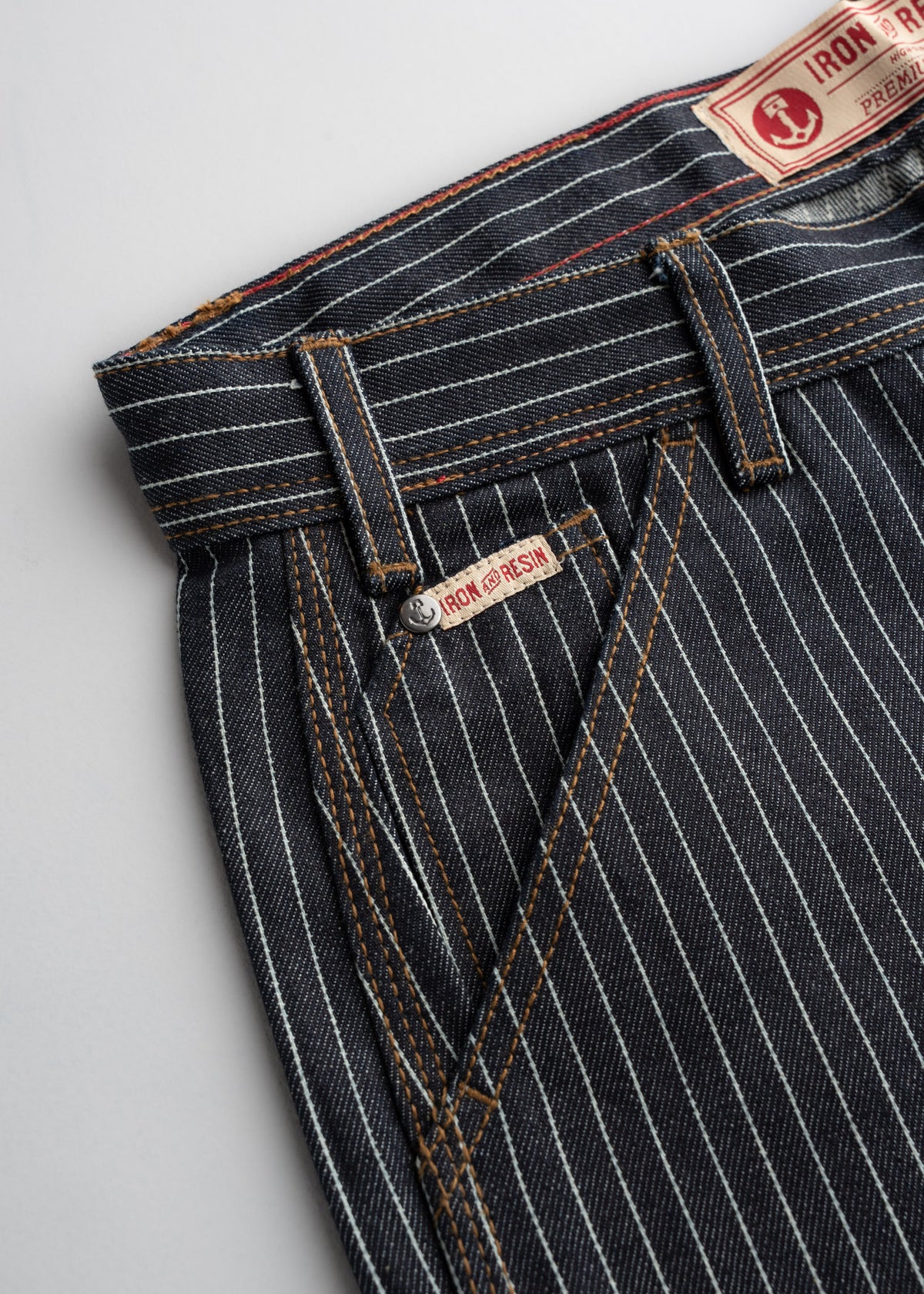 Close up of waistband construction on denim pants, showcasing pockets, stitching and engraved button detail