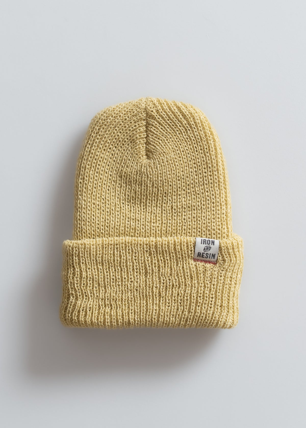 A beige knit beanie with a folded brim and "Iron and Resin" label, placed on a plain white background.