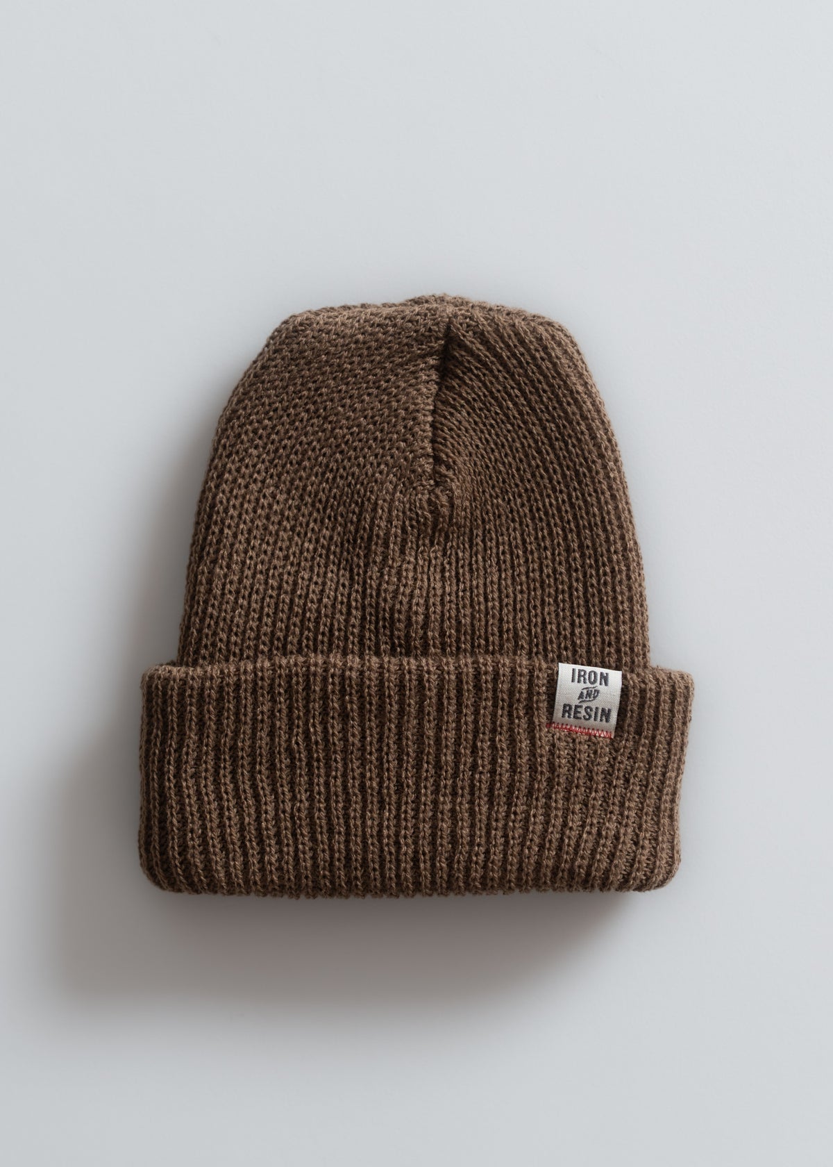 Brown knit beanie with "Iron and Resin" label on a light gray background, showcasing its simple, cozy design.