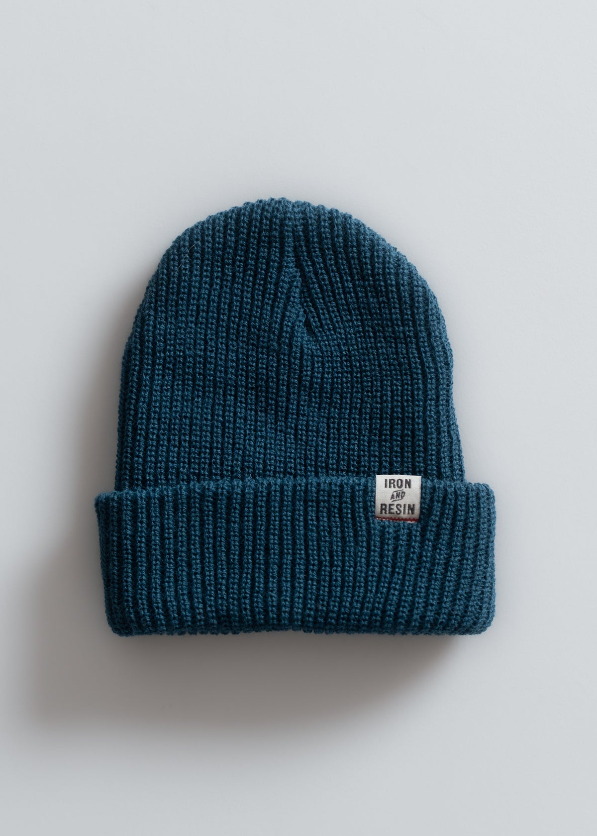 Blue knit beanie with a folded brim, featuring an "Iron and Resin" label, set against a plain white background.